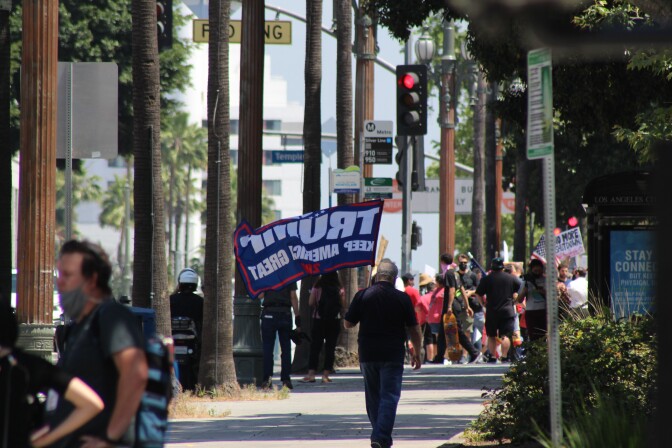 Man with "Trump 2020" flag walks down street, towards other protestors on May 1 in Downtown L.A. | Karen Foshay