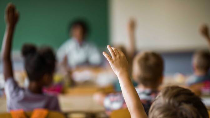Children raising their hands in a classroom, iStock