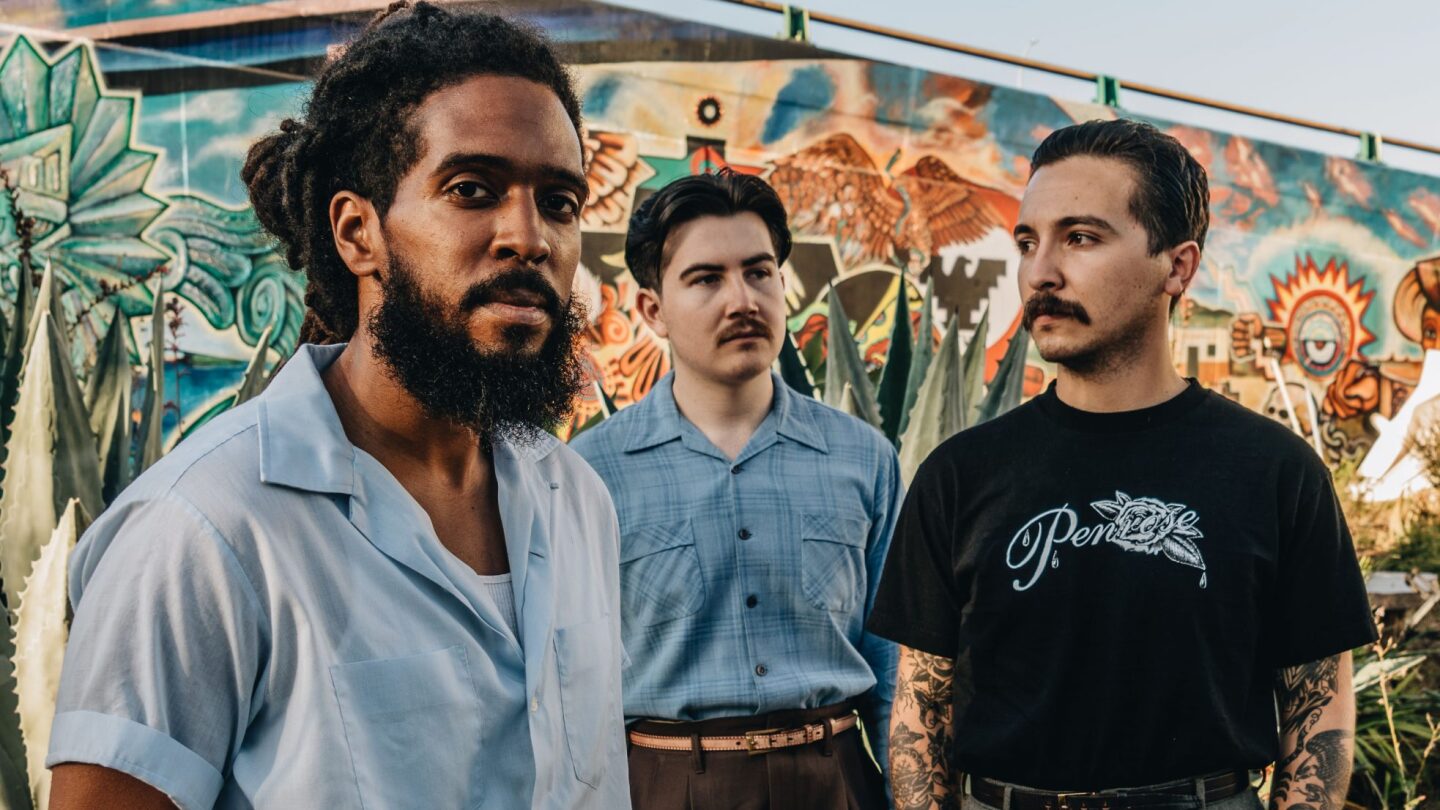 The members of Thee Sacred Soul stand together in front of a mural.