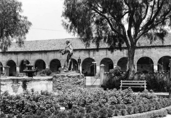 A pepper tree stands near a statue of a missionary at the San Fernando Mission. Courtesy of the USC Libraries - California Historical Society Collection.