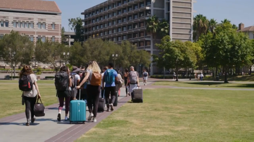 A group of college students with their suitcases make their way across the USC campus.