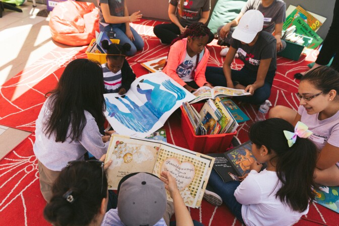 Children sitting on a mat reading books with parents and caregivers. | PBS SoCal
