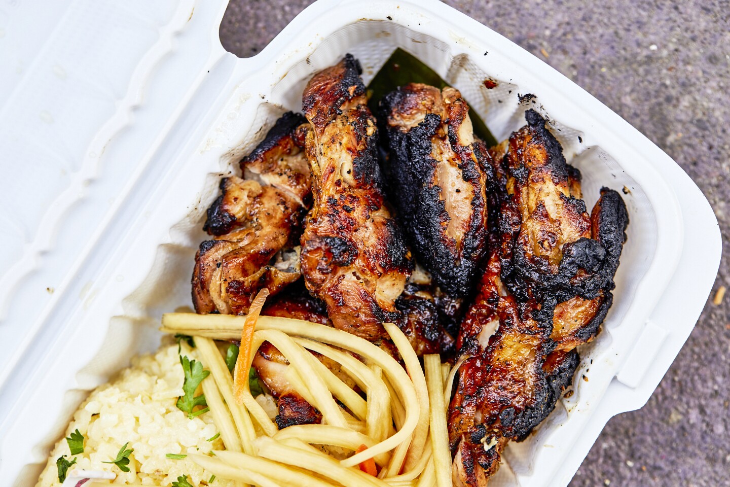 Chicken inasal, grilled chicken, from Mano Po over a bed of rice and packaged in a white to-go box.
