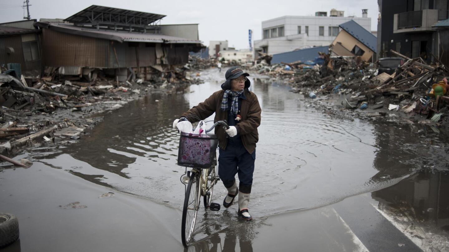 A resident of a Japanese town pushes his bike through a flooded street lined with wreckage. | From "NOVA: Japan's Killer Quake"