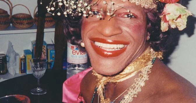A person with a large smile wears red lipstick and a crown of flowers.