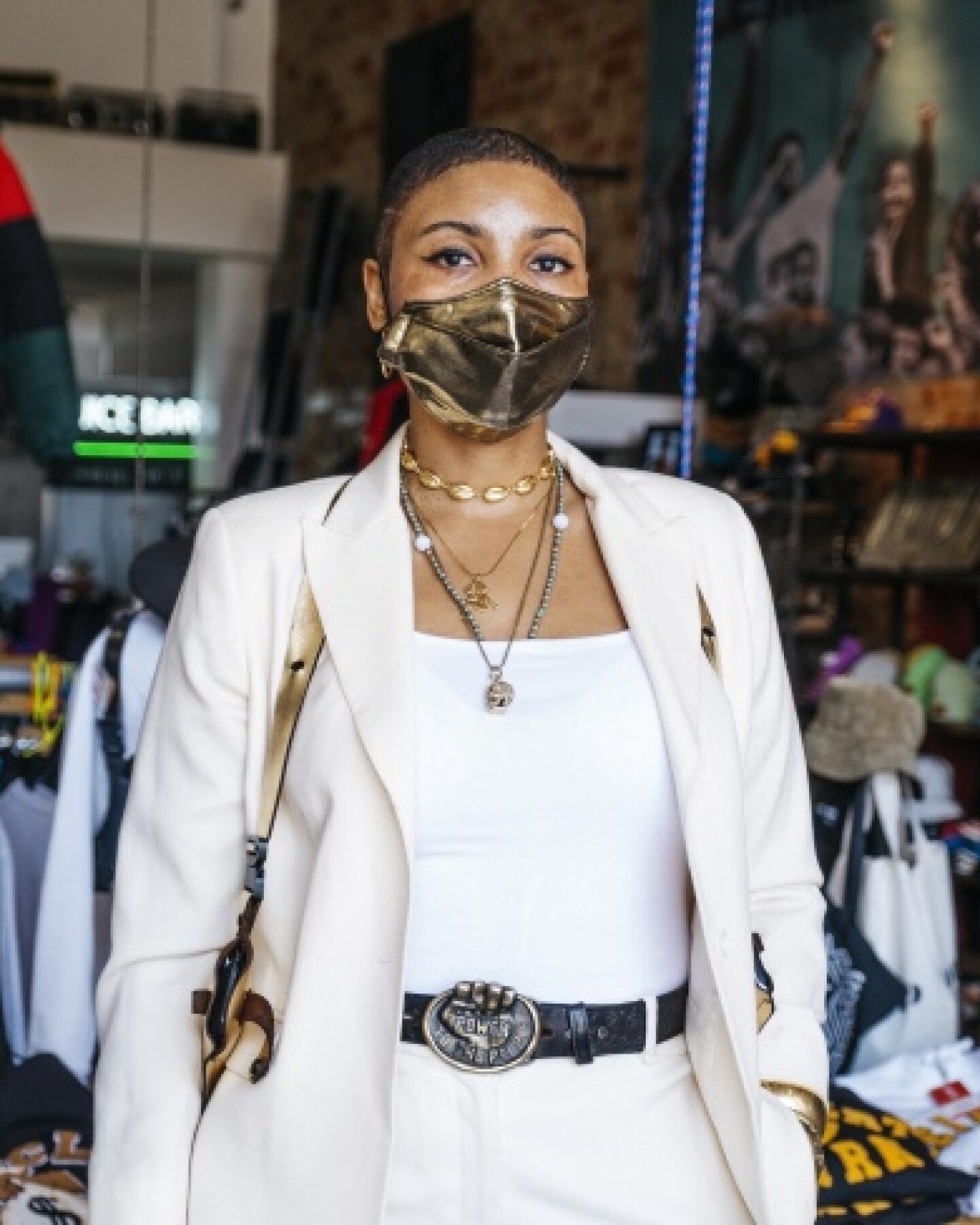 A woman in a shiny face mask and white suit in front of a clothing store