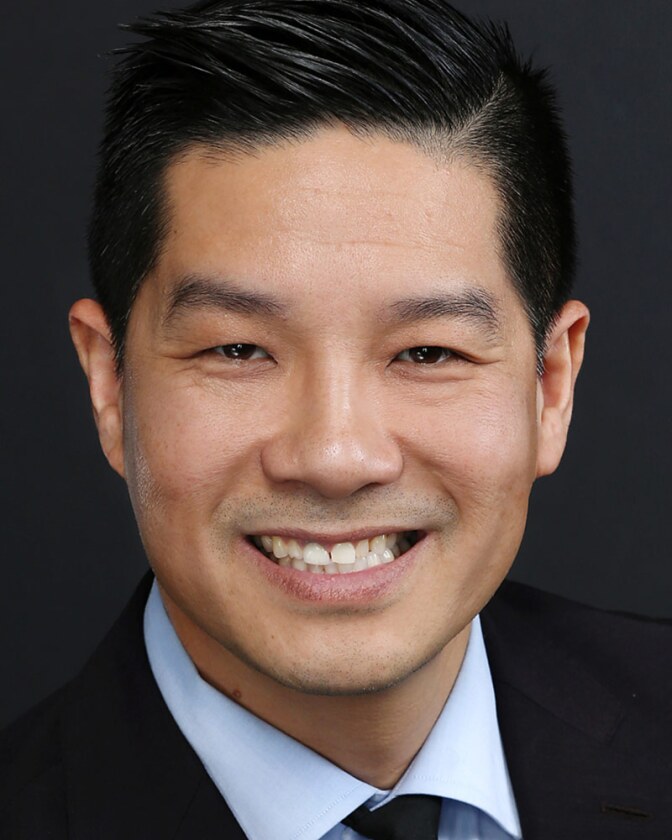 Tam Nguyen smiles in a suit and tie