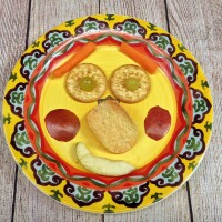 A smiley face made out of food items on a yellow paper plate