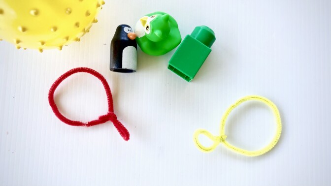 two craft pipe cleaners bent to resemble the shape of magnifying glasses are on a table next to several small toys.