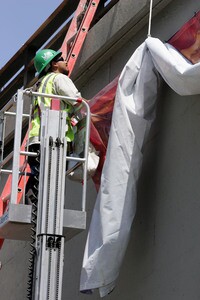 Worker hang a banner with an image of a former 101 Freeway mural. Rolled up, it was stolen after being installed. I Caltrans