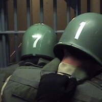 Men in Green Body Armor and Hardhats Gather in Front of Cell Bars