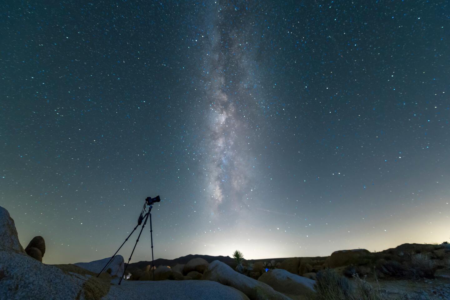 A night sky at Joshua Tree shows the Milky Way and a camera on a tripod.