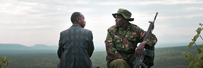 A man in civilian clothes looks at another man wearing an army uniform and resting a rifle in his arm. | "When Lambs Become Lions"