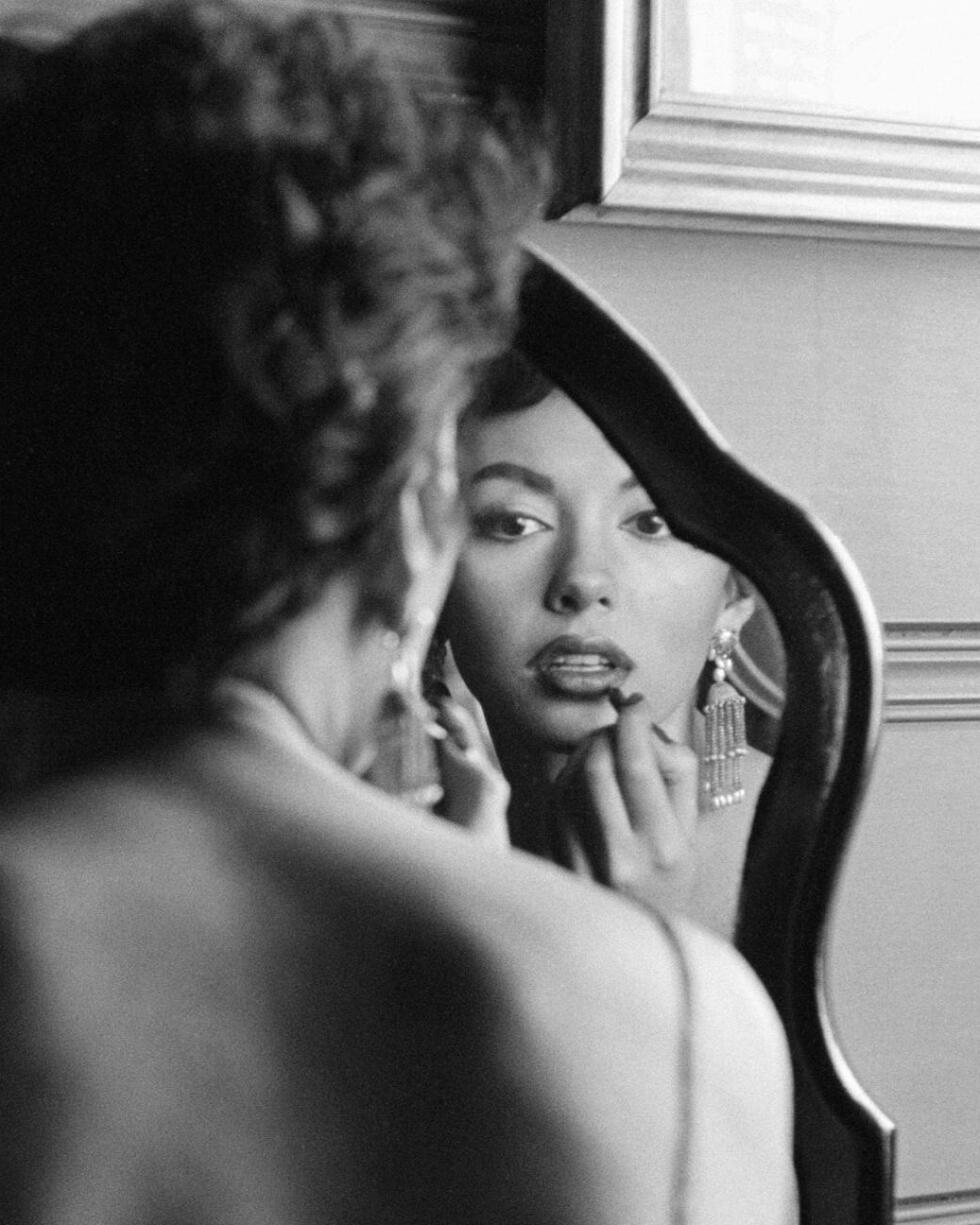 Rita Moreno facing a mirror draws on her lipstick.