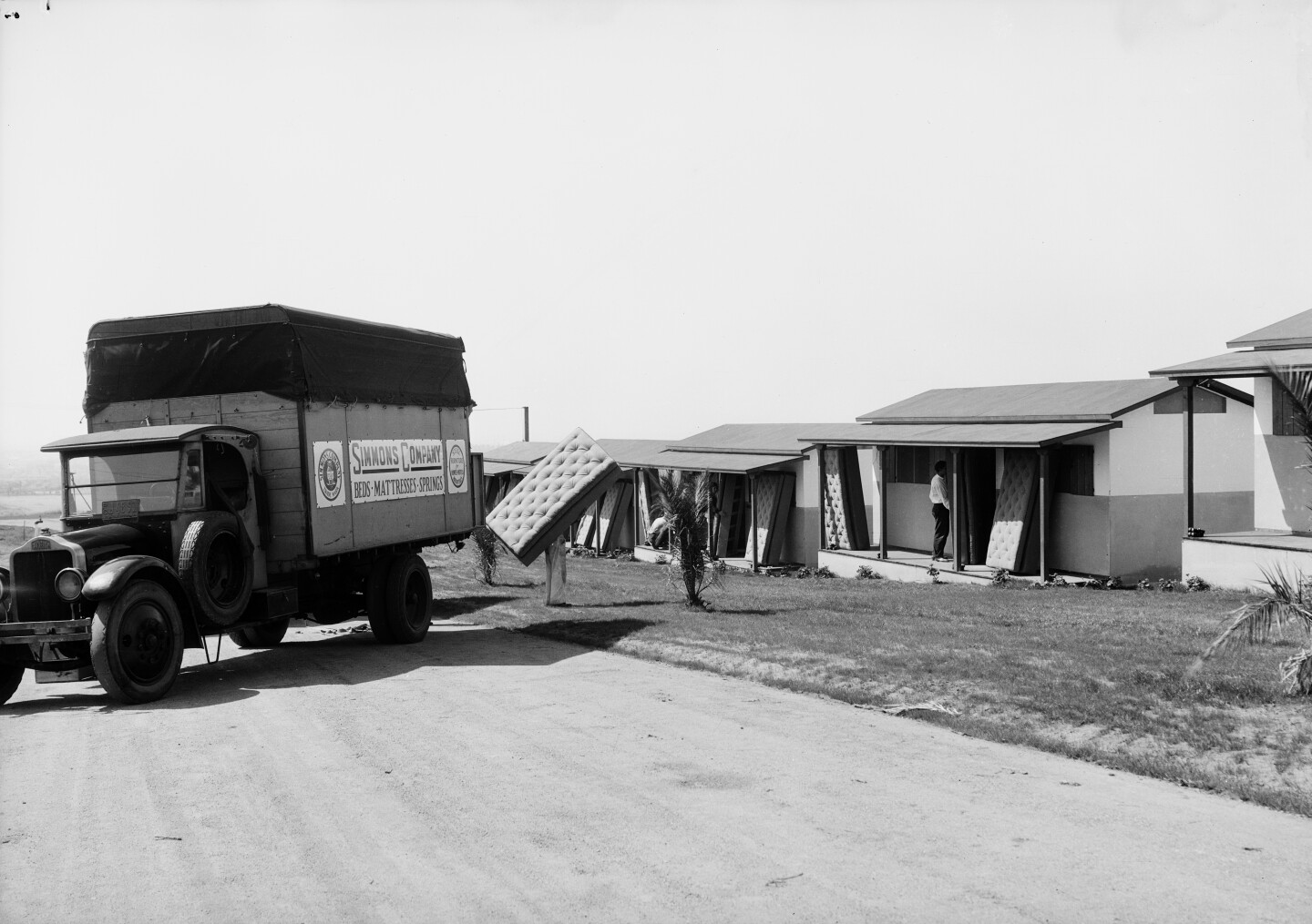 A bed cushion is carried by a man walking into one of the homes in the Olympic village during the 1932 Los Angeles Olympic Games.