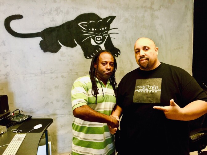 Two African American men shake hands in front of a Black Panther-designed wall.