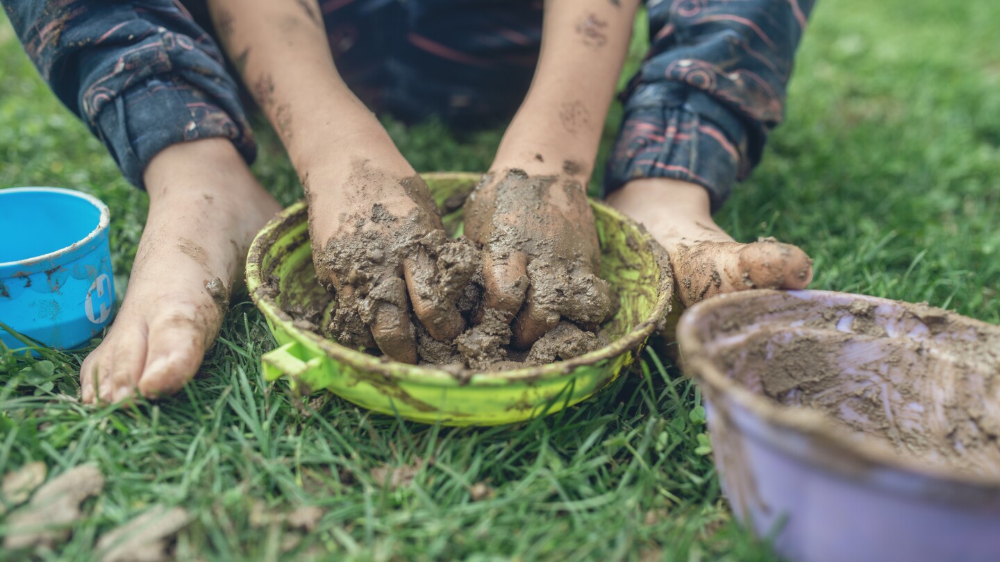 Image of toddler child sitting in grass playing with mud having his hands and feet all dirty.