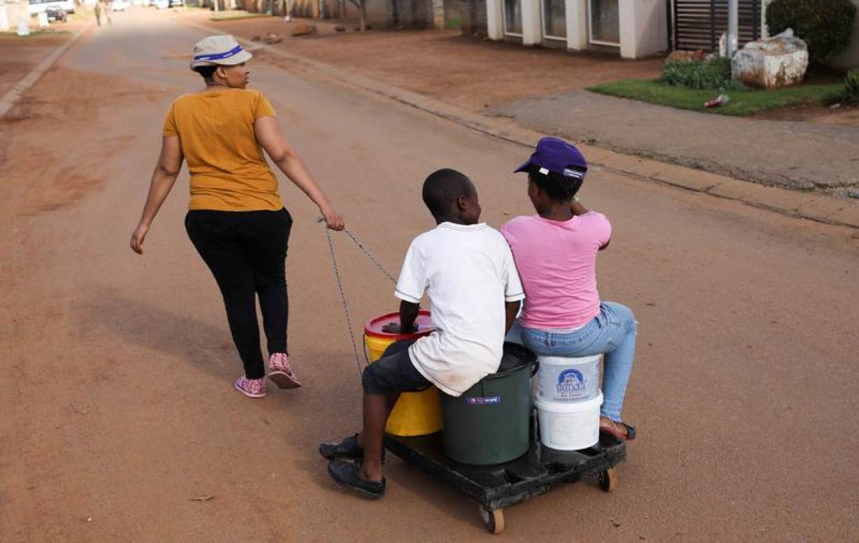 Children sit on a trolley with buckets as the mother pulls it on their way to collect water from a nearby church, as their community experiences water cuts during a nationwide lockdown for 21 days to try to contain the coronavirus disease (COVID-19)
