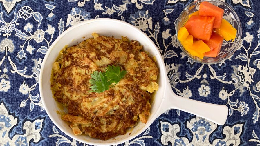 A small white skillet with an egg pancake in it with a small glass cup of fruit next to it