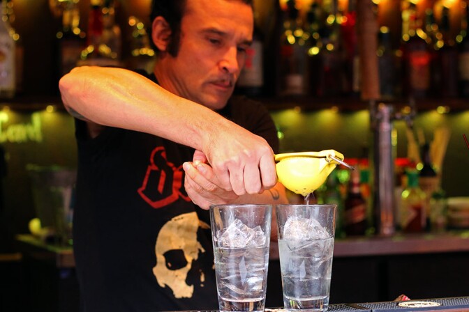 A bartender squeezes a fruit into two drinks.