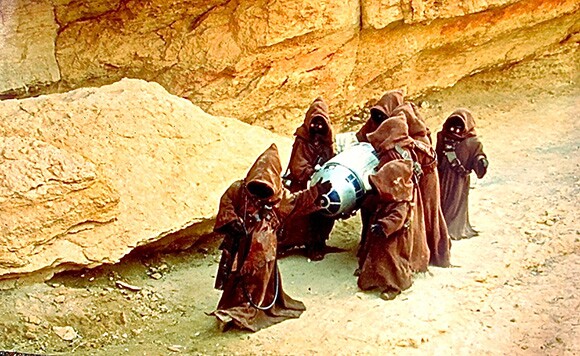 Jawas carrying R2-D2 in a desert landscape.