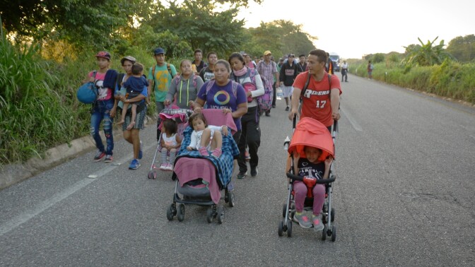 A group of migrants in a caravan push strollers on the road.