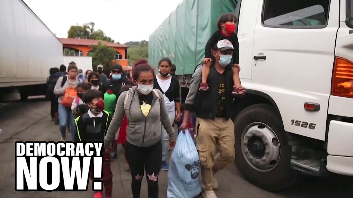 A long line of people wearing face masks walk between two parked trucks.