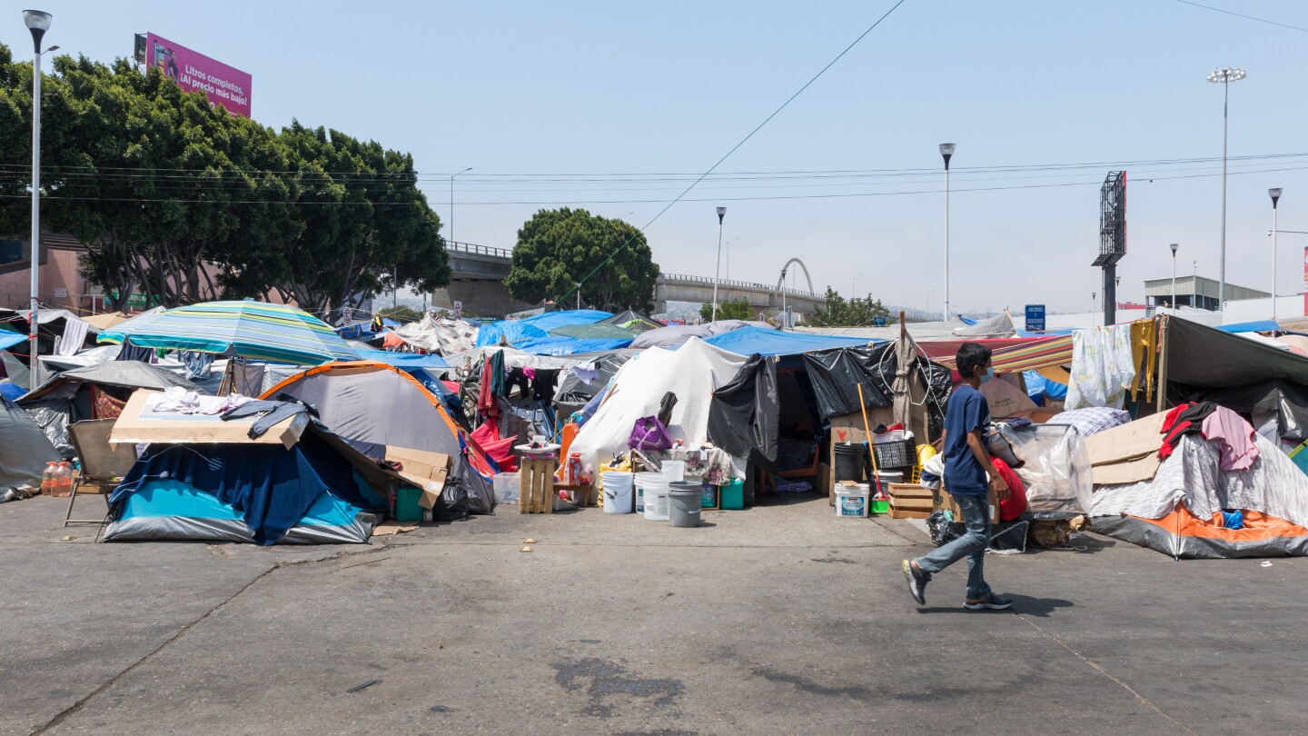 An asphalt surface is covered in various encampments. A boy is walking across the frame.