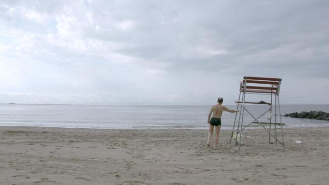 A man in swimwear at an empty beach faces the ocean. | From "Independent Lens: The Hottest August"