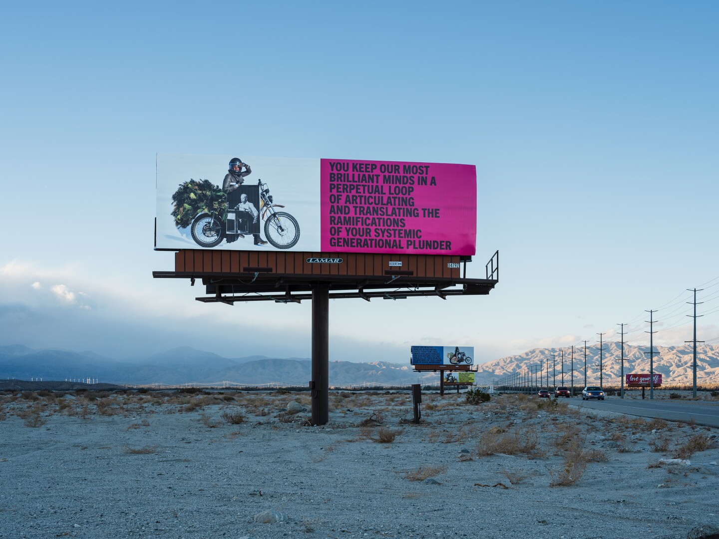 Simmons' billboards stand along the Gene Autry Trail. The one photographed reads, "You keep our most brilliant minds in a perpetual loop of articulating and translating the ramifications of your systemic generational plunder."