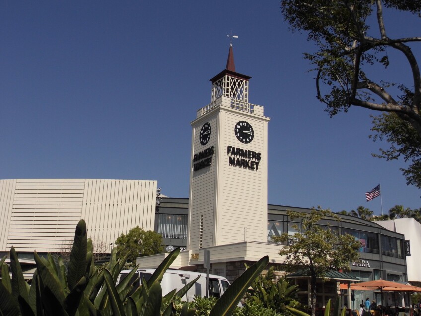 A clock tower with the words FARMERS MARKET rises above a shopping center, with a ZARA store in the background