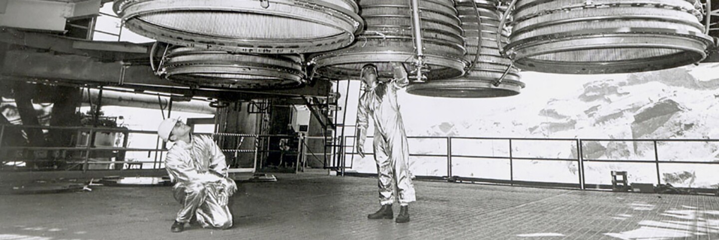 Two workers are dwarfed by five Rocketdyne J-2 engines of the Saturn V second stage (S-II) as they make final inspections prior to a static test firing by North American Rockwell’s Space Division. | Courtesy of NASA