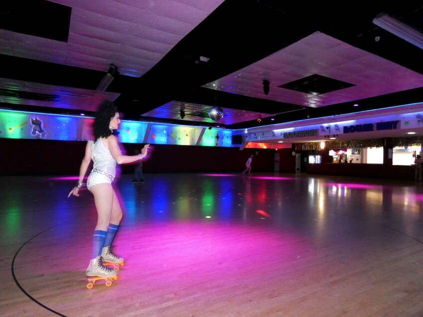 A woman in rollerskates and disco clothing skates inside the Moonlight Rollerway in Glendale.