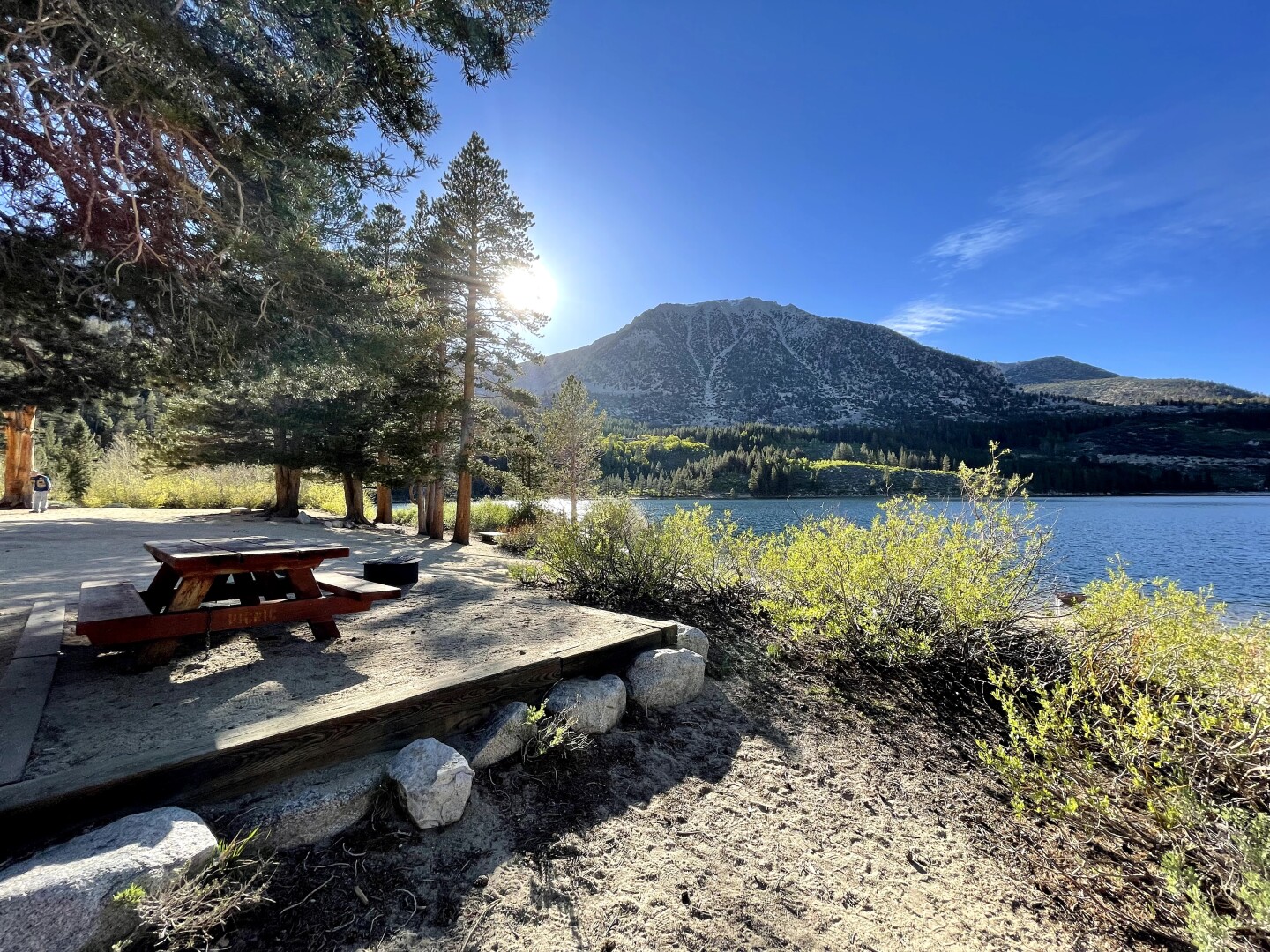 A clear lake on the right with an elevated space that has a bench.