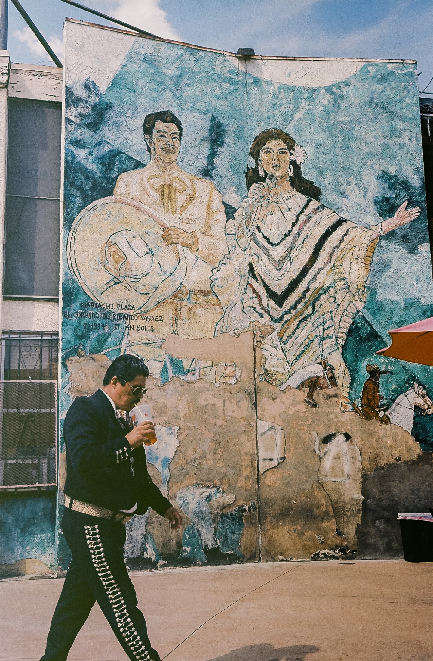 A Mariachi musician passes in front of a mural honoring Mariachi Plaza in Boyle Heights.