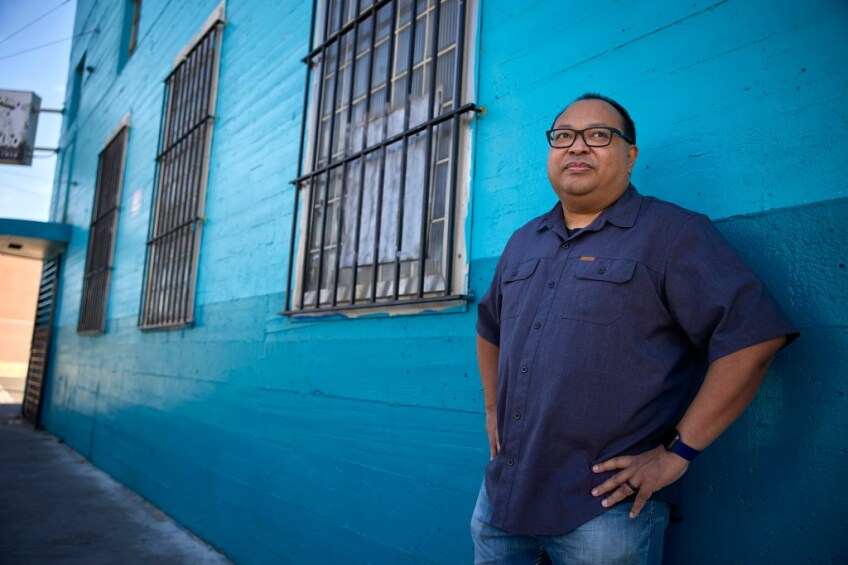 Dillion Delvo stands in front of a blue building with gated windows.