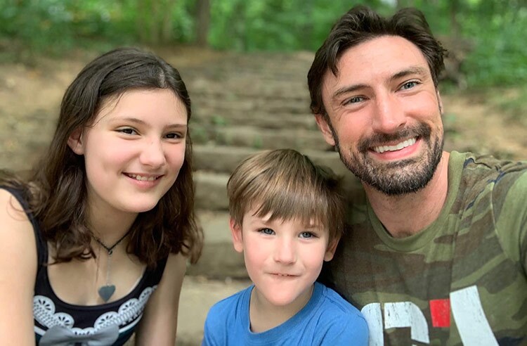 A white family composed of an older girl, small boy and a father, smile at the camera