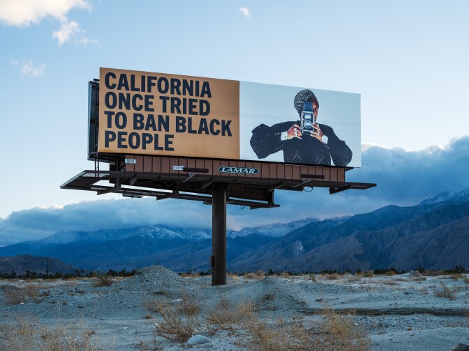 One of Simmons' billboards reads, "California once tried to ban Black people." To the right of the text is a Black woman holding a vintage camera.