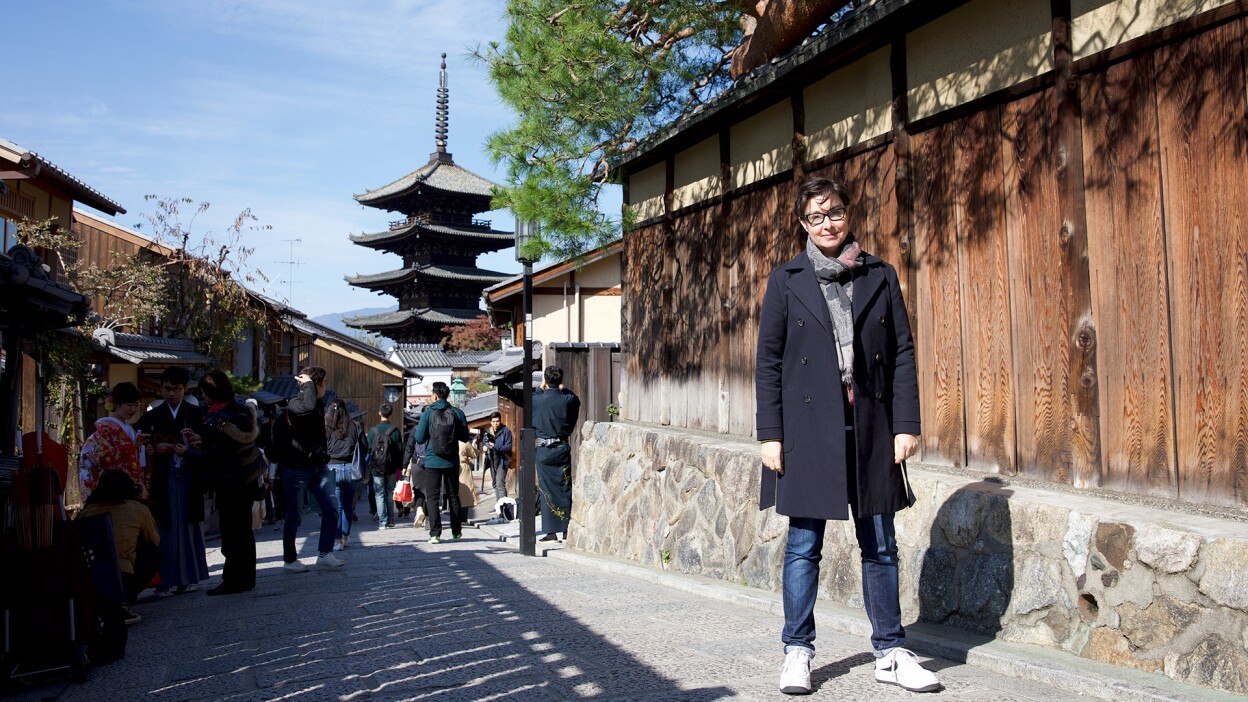 Sue Perkins stands in a small street in Japan with a pagoda in the background. | From "Japan with Sue Perkins"