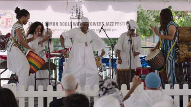 A group of performers dance and drum at the Day of the Drum Festival at the Watts Towers Arts Center. | Still from "Southland Sessions" " Watts Towers Festivals"