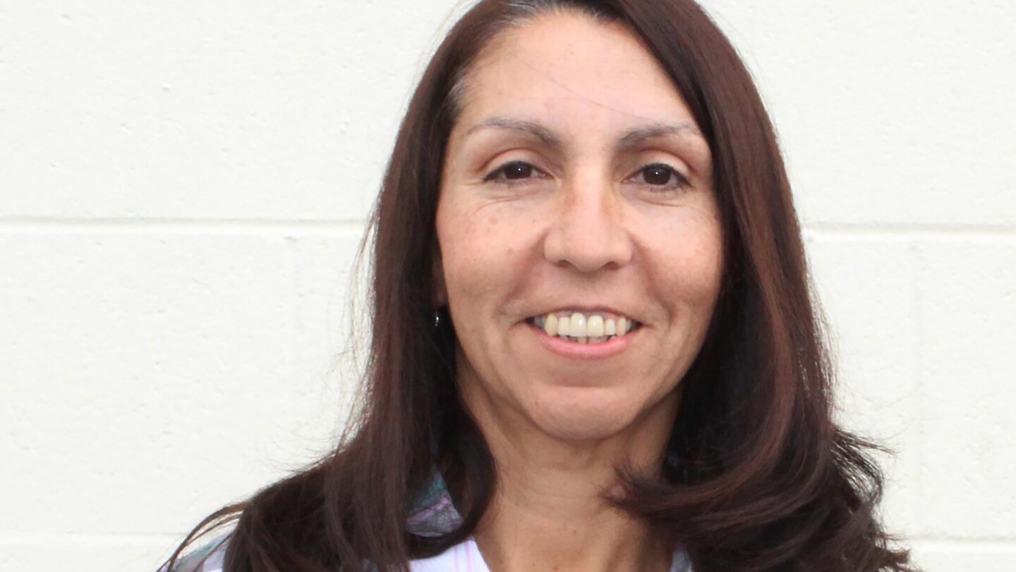 Frances Montoya wears her long brown hair down and smiles at the camera in a purple plaid shirt.