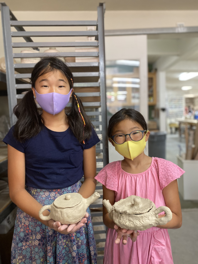 Two young Asian American girls hold their ceramic teapots