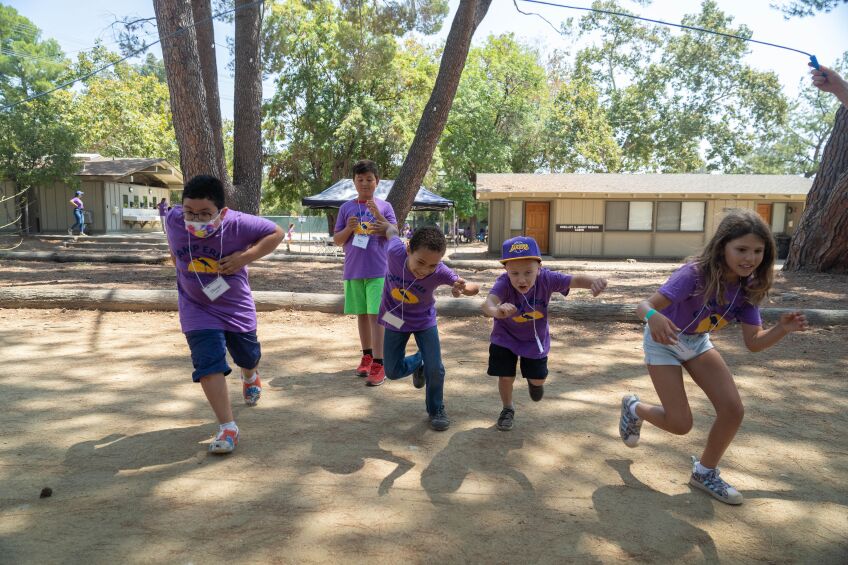 cinco niños en camisetas moradas iguales bailan al aire libre.