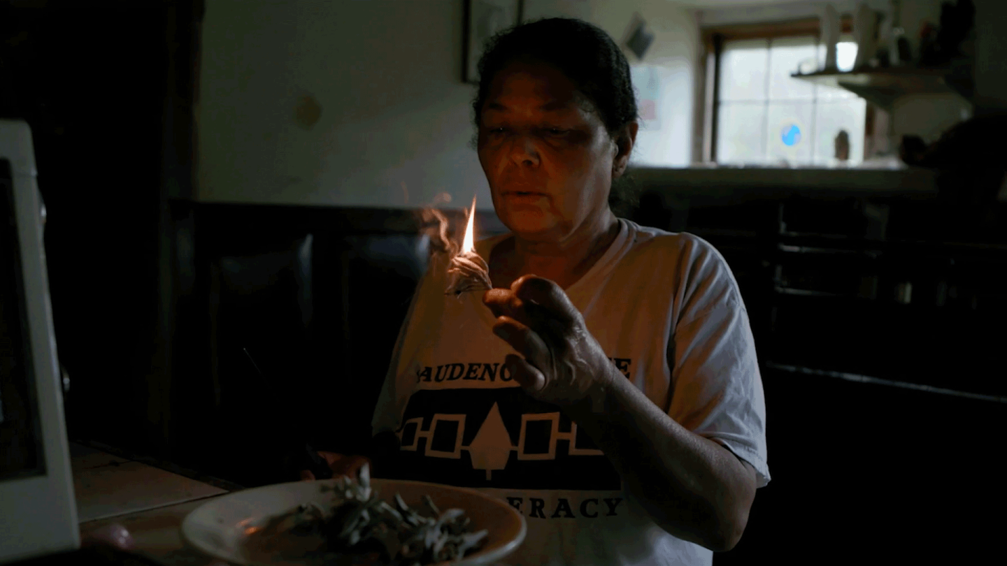 A woman gently blows on a flame in a low lit room. | From "Independent Lens: Conscience Point"