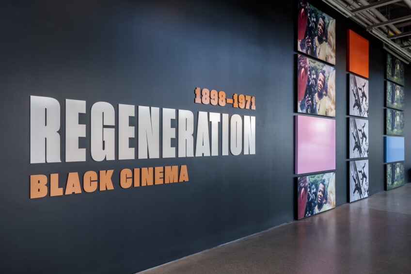 On a black wall, the word, "Regeneration" is prominently displayed. Below it reads, "Black Cinema" and above it it reads, "1898-1971." To the left, various still images from films are arranged vertically. 