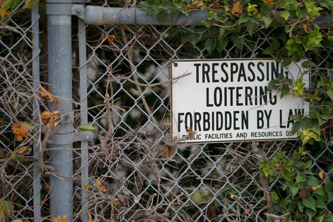 A sign on a fence reads "Trespassing loitering forbidden by law."