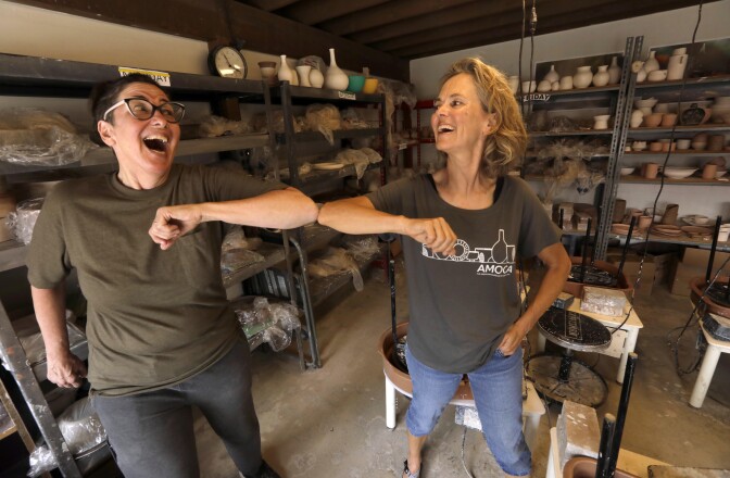 Two people bumping elbows in a room full of ceramics.