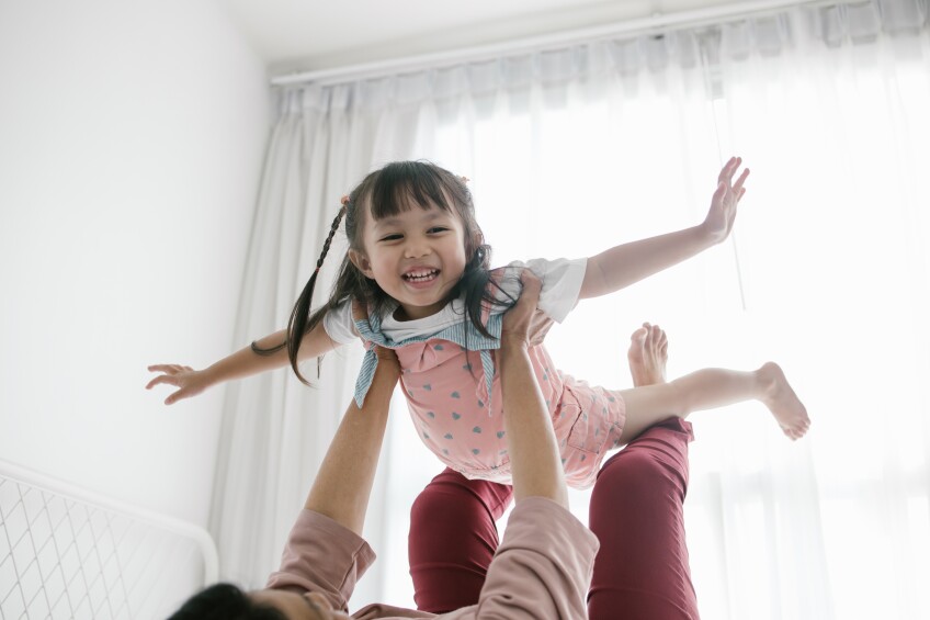 A small girl is lifted up off a bed by her caregiver and she pretends to fly