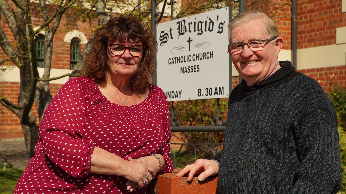 Linda Lawless and former Catholic priest Peter Finn pose in front of a sign for St. Brigid's church.