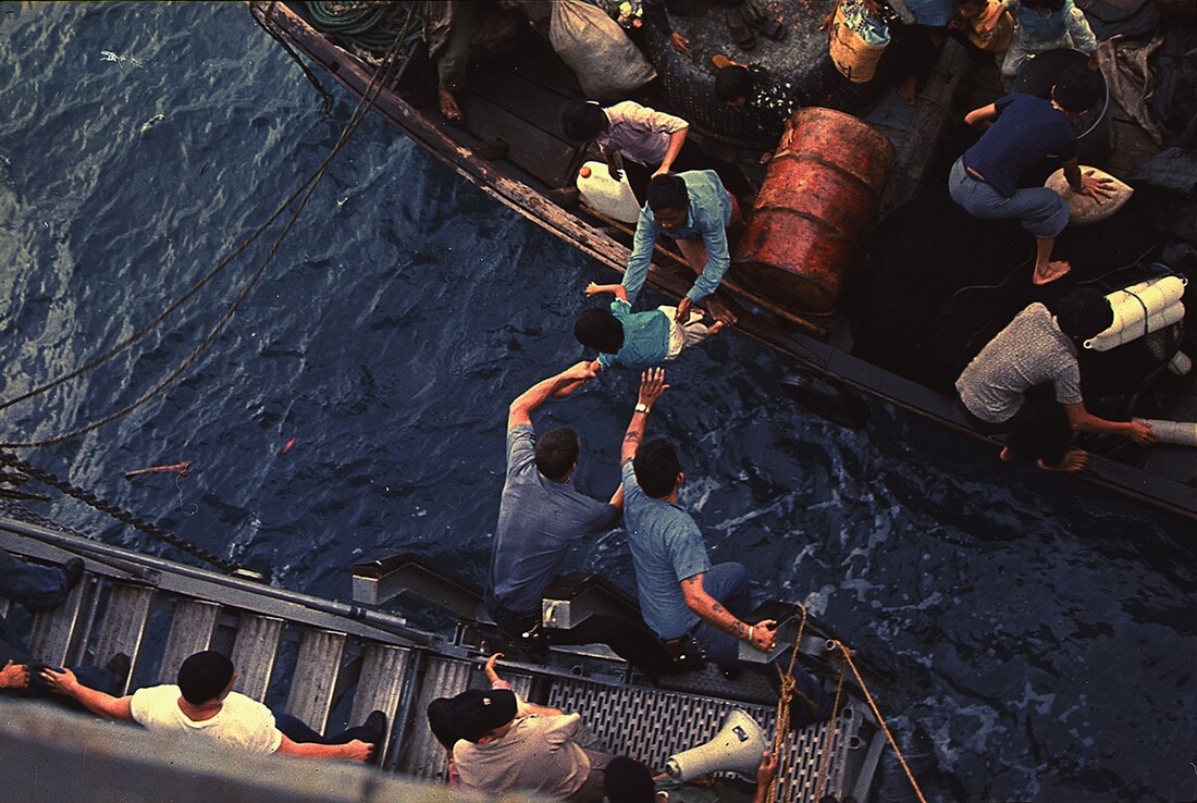 Crewmen of the amphibious cargo ship USS Durham (LKA-114) take Vietnamese refugees aboard a small craft. South China Sea, 1975. | National Archives and Records Administration